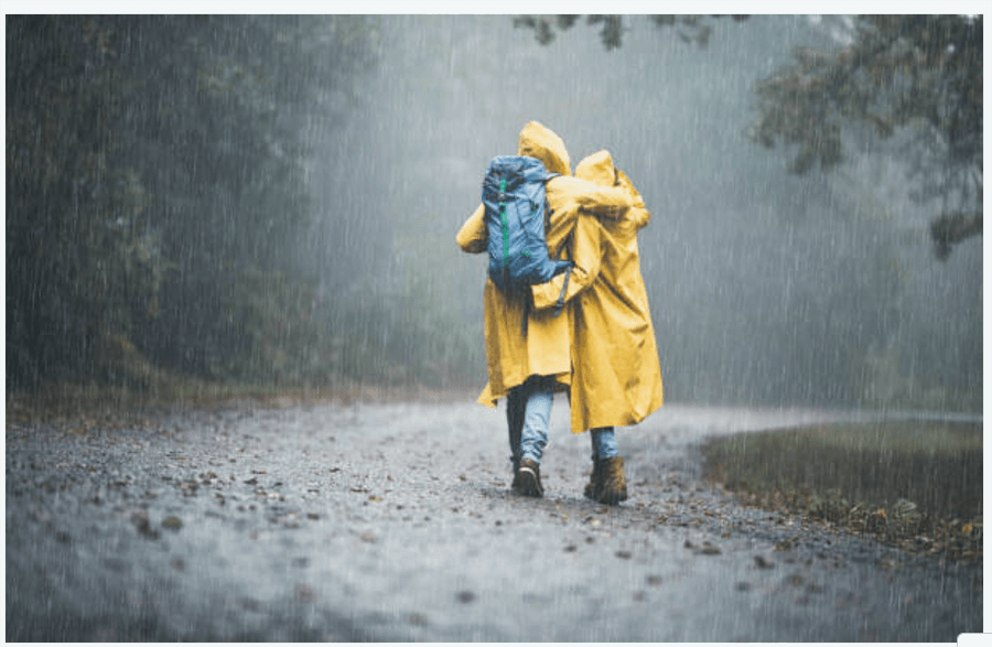 A couple hiking a trail in heavy rain, wearing raincoats and hiking boots for muddy terrains
